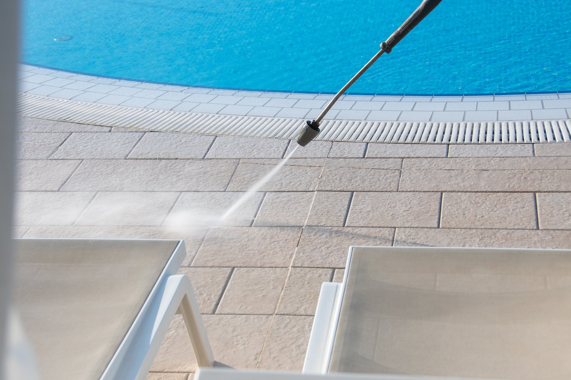 High-pressure water jet cleaning tiles around swimming pool